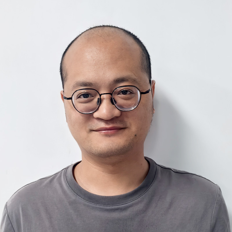 Smiling man with glasses in a gray t-shirt, professional corporate headshot of Alen Chen, R&D Product Manager.