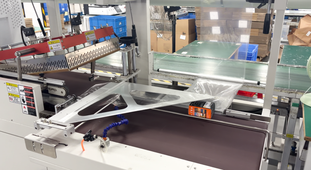 ETENWOLF AIR-3 box entering an automated shrink wrapping machine on a factory assembly line.