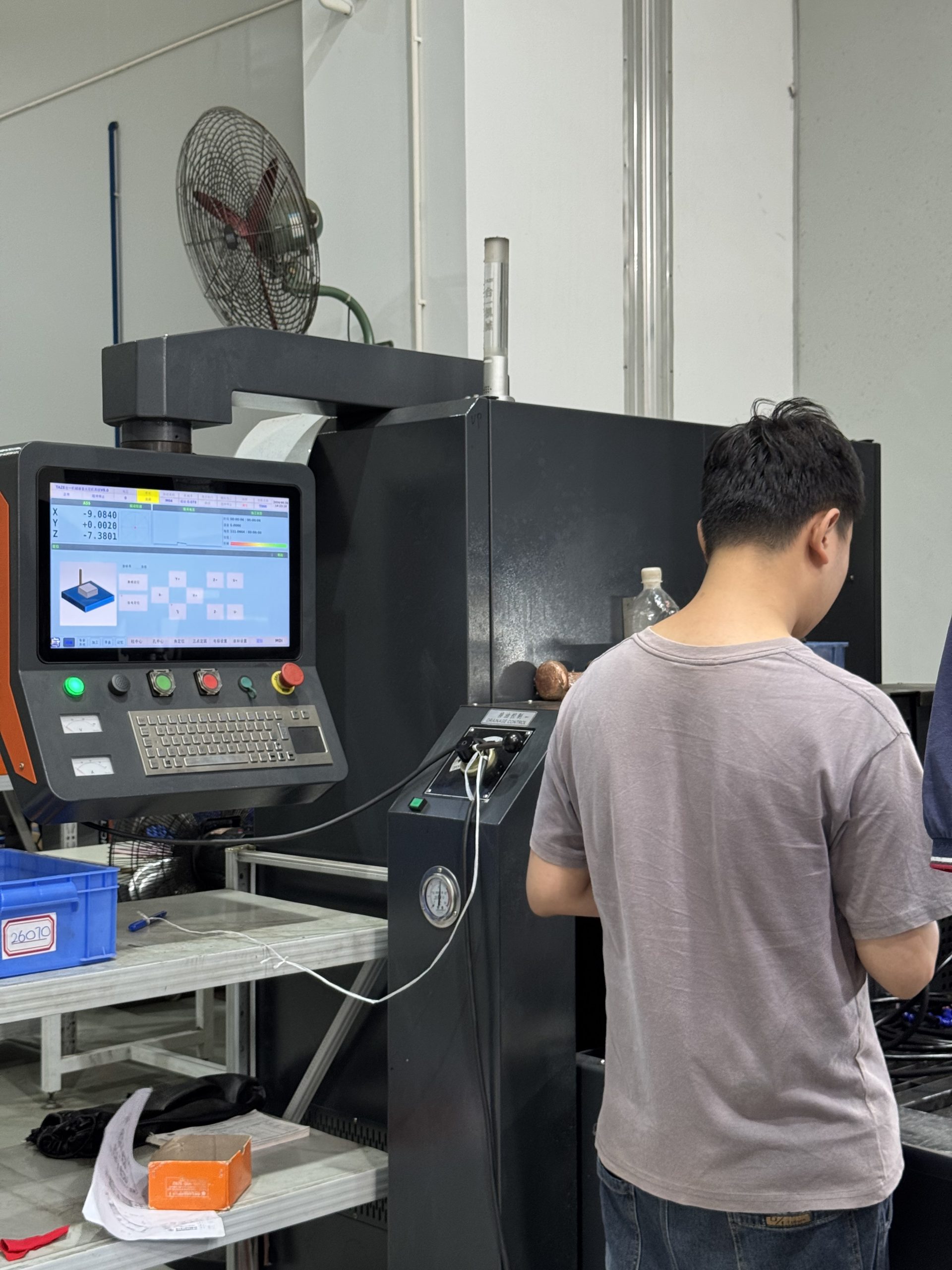 A TAZE CNC-1260 EDM machine control panel displaying three-axis machining coordinates, with an operator working next to it at the ETENWOLF workshop.